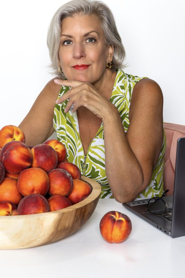 A woman sitting at the table with peaches in front of her.